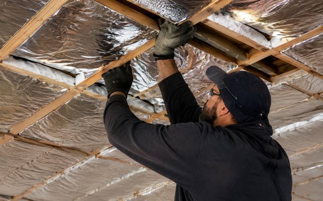 Installer fastening foil-faced insulation to the underside of sloped roof rafters