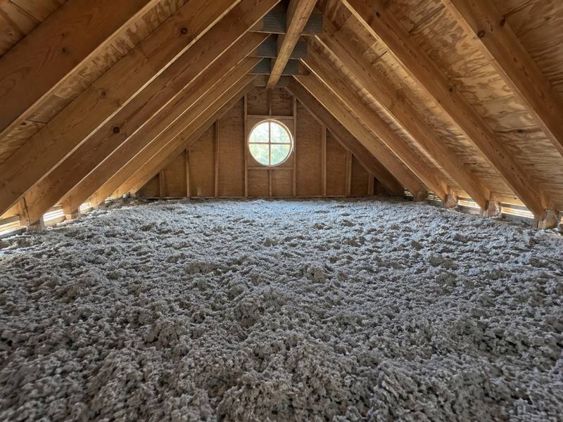 Grey blown-in cellulose spread evenly across a whole attic, with a round gable window at the far end